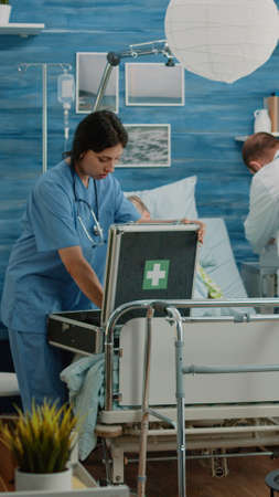 Worried man asking medical team to help sick old wife in nursing home. Doctor and nurse rushing to give assistance to ill retired patient hyperventilating, laying on hospital bedの写真素材