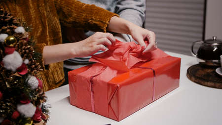 Close up of hand decorating present box with wrapping paper and bow with ribbon. Festive woman preparing gift for family, using ornaments for christmas eve celebration. Winter festivityの写真素材
