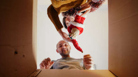POV of man and woman opening box with garlands and ornaments, decorating for christmas eve. Festive...