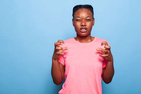 Portrait of annoyed african american teenager holding hands in furious gesture standing in studio with blue background. Unhappy young woman having negative emotion at camera. Dissatisfied conceptの写真素材