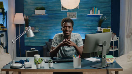 Portrait of black adult sitting at desk with computer and notebook. Man of african ethnicity looking...