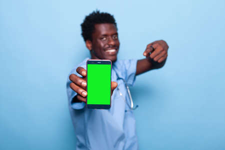 Nurse showing smartphone with vertical green screen. Medical assistant holding device with chroma key and mockup template for isolated background on display. Man with modern phoneの写真素材