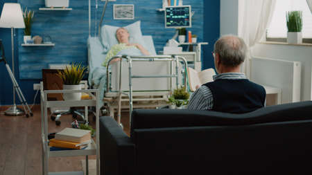 Aged man calling for doctor and nurse to help sick woman in hospital bed. Patient with disease breathing heavy while medical team running to give assistance and support for healthcare.の写真素材