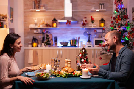 Happy family sitting at romantic dining table in xmas decorated kitchen enjoying christmas dinner together. Cheerful people enjoying winter holiday season celebrating christmastimeの写真素材