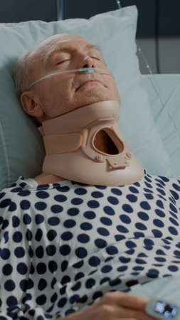 Portrait of elder patient sitting with cervical neck collar in hospital ward bed at intensive care...