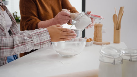 Closeup of grandmother hands putting flour in strainer while granddaughter sift ingredient in kitchen bowl preparing xmas homemade cookie dessert. Family celebrating christmas enjoying winter holidayの写真素材