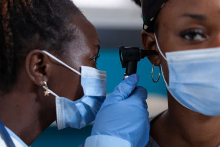 Closeup of african american otologist doctor with protective face mask against coronavirus checking...