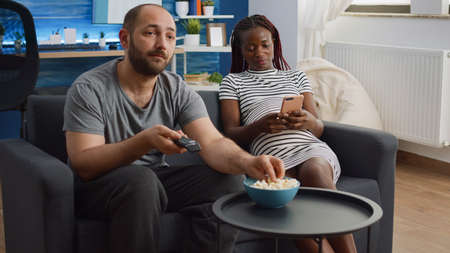 Modern interracial family expecting child using technology in living room. African american pregnant...