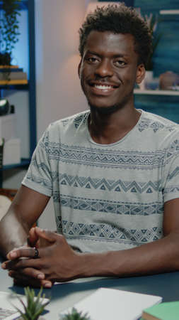 African american man smiling and working on laptop while looking at camera. Portrait of business person sitting at desk with notebook and modern device for office work. Black adultの写真素材