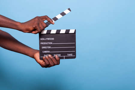 Close up of hand holding clapperboard in studio. Person with chalkboard used to cut scenes for...