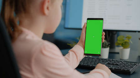 Close up of child holding green screen on smartphone for homework and school tasks. Young girl...