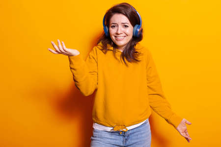 Positive adult feeling excited and listening to music on headphones. Happy young woman smiling and looking at camera while enjoying song and sounds on headset. Adult having entertainmentの写真素材