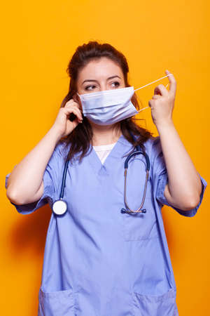 Medical assistant putting on face mask for protection in front of camera. Woman nurse with uniform...