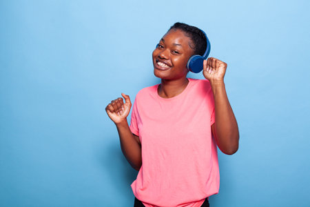 Portrait of african american teenager dancing alone in studio with blue background enjoying song...