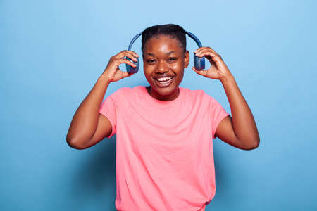 Portrait of carefree african american young woman putting headphones smiling at camera listening...
