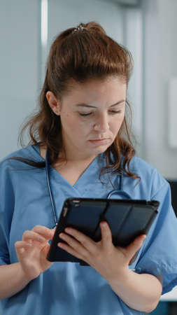 Close up of medical assistant looking at tablet screen with information for healthcare system in cabinet. Portrait of nurse specialist using gadget with touch screen for practice.の写真素材