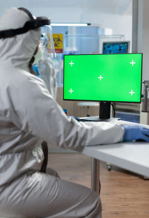 Microbiologist researcher with protective medical equipment analyzing vaccine expertise looking at mock up green screen chroma key computer with isolated display. Biology hospital laboratoryの写真素材