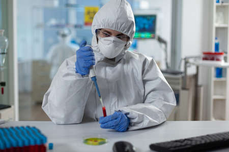 Scientist woman analyzing blood using medical micropippete during vaccine development working in microbiological hospital laboratory. Researcher wearing ppe suit during clinical experimentの写真素材
