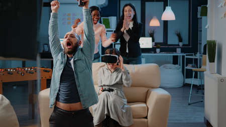 Workmates playing video games with controller on console after work at office. Woman winning game...