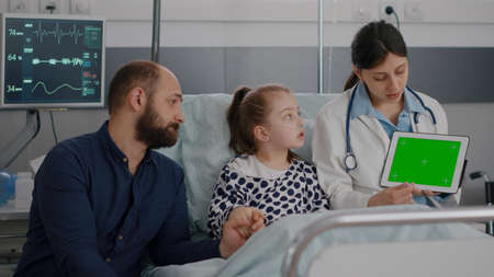 Pediatric doctor explaining sickness symptoms discussing surgery procedure during recovery medical examination. Worried dad sitting beside daughter in hospital ward waiting for medication treatmentの写真素材
