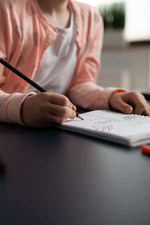 Closeup of little schoolchild writing mathematics homework on notebook during classroom lesson...