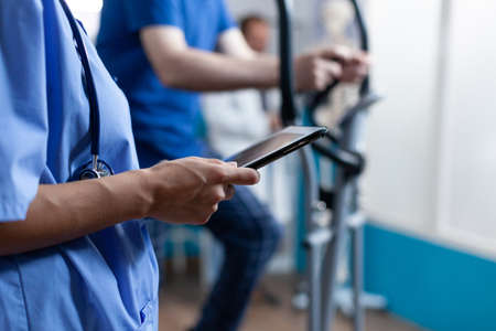 Close up of nurse holding digital tablet with touch screen at recovery clinic. Medical assistant...