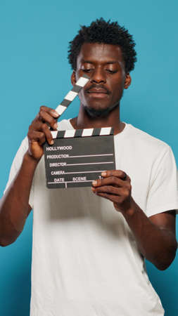 Portrait of man holding clapperboard to cut scenes in movie industry. Cheerful person using chalkboard for film making production and cinematography in studio. Young adult with clap boardの写真素材