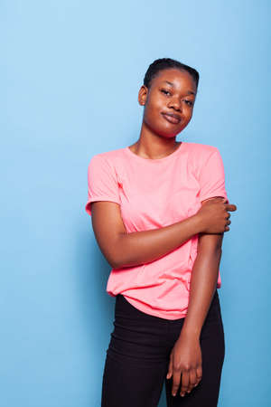 Portrait of african american young woman smiling at camera standing posing during photography session standing in studio. Friendly joyful teenager over blue background. Relaxation conceptの写真素材