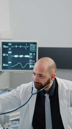 Doctor using stethoscope for heartbeat measurement on sick patient in hospital ward bed. Medic doing...