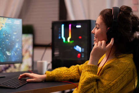 Focused smiling woman gamer discussing with players using streaming headphones playing space shooter...