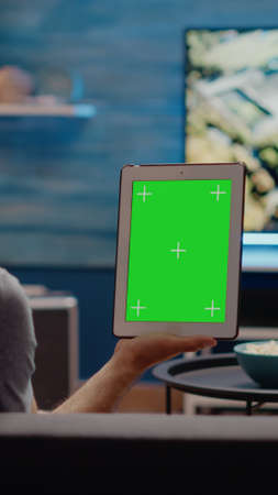 Young man vertically holding digital tablet with green screen design in living room. Modern...