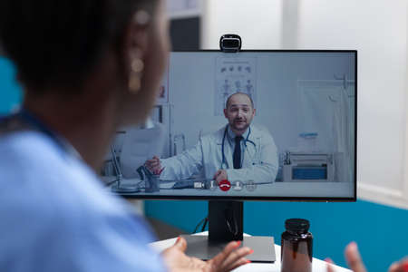 African american asisstant discussing flu symptoms with remote physician doctor during online...