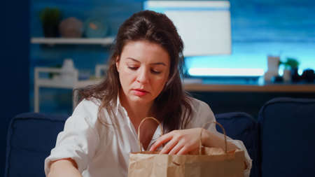 Close up of businesswoman with takeaway food order on table taking fast food meal out of bag to eat...