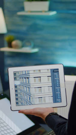 Architect holding digital tablet with building model for construction layout in office. Man engineer working on blueprint plan with touch screen monitor and device for architectural projectの写真素材