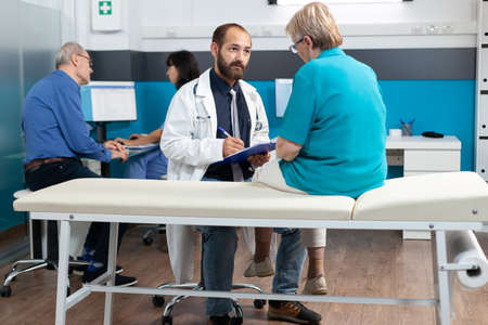 Elder patient discussing with doctor about osteopathy and injury at healthcare consultation. Medic...