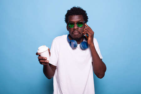 Casual person with sunglasses raising shoulders and chatting on phone call. Joyful man talking on...