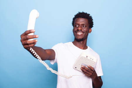 African american man pretending to take selfie on old landline phone. Black person having fun with...