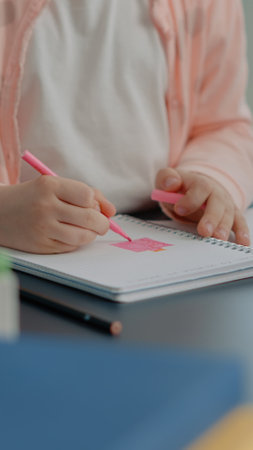 Close up of young child using colorful pencils on notebook at desk. Little girl holding pen to draw...
