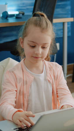 Young child using keyboard on laptop for homework and online courses for distance education. Little...
