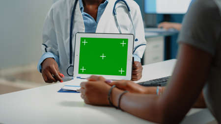 Close up of horizontal green screen on digital tablet at checkup visit. Doctor pointing at mockup...