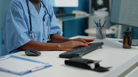 Close up of medical assistant typing on computer keyboard in cabinet for appointments with patients. Woman nurse using monitor and technology for healthcare system and receptionの写真素材