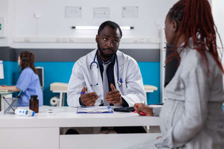 African american doctor and patient with pregnancy talking about healthcare and support. Specialist giving medical advice to young woman expecting child, preparing to give birth.の写真素材