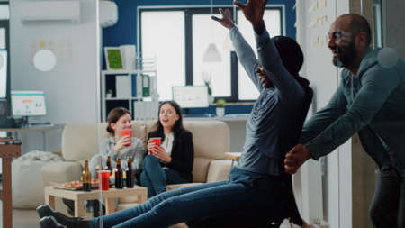 Man and african american woman having fun at office after work. Workmates enjoying free time with drinks and alcoholic beverage for entertainment after hours. Colleagues smilingの写真素材