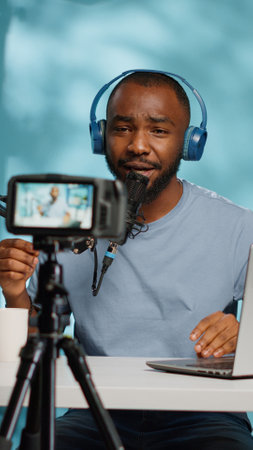 African american vlogger using camera to record video in studio while using microphone and podcast equipment. Black influencer filming vlog for social media channel, wearing headphones.の写真素材