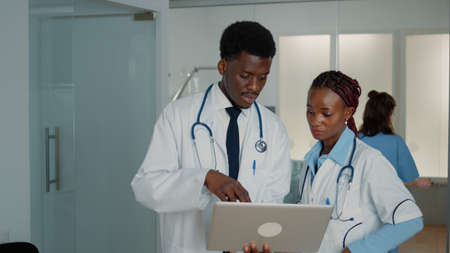 Team of african american doctors working with laptop to cure patient with disease, searching for...