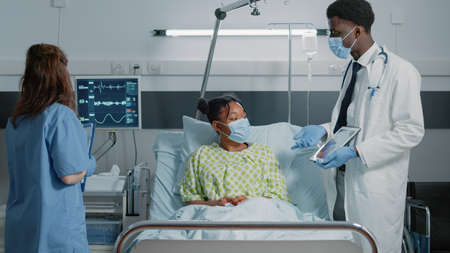 Physician pointing at tablet with cardiology diagnosis to explain disease to woman during pandemic. Doctor showing cardiovascular image on display to give medical assistance to patientの写真素材