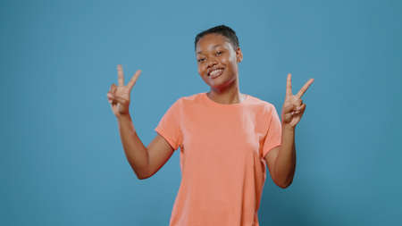 Cheerful woman doing peace symbol with fingers and smiling in front of camera. Positive adult...