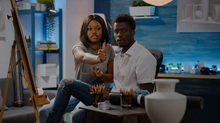 Couple of african american artists drawing white vase for authentic fine art sitting in workshop at home. Black man and woman working with tools, pencils, canvas and easel for masterpieceの写真素材