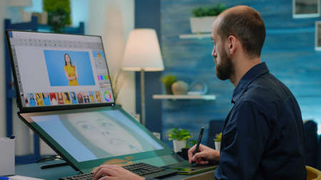 Photography artist editing photos with graphic tablet and stylus while using touch screen monitor with retouching app. Man photographer doing retouch work on pictures for media project.の写真素材