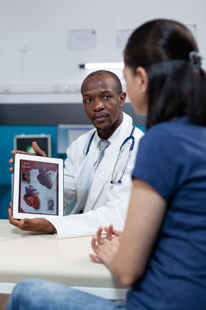 African american pediatrician doctor holding tablet computer in hands with heart radiography on...